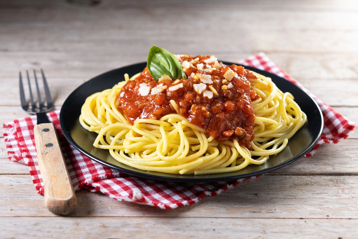 A plate of Spaghetti Bolognese garnished with fresh Parmesan cheese.